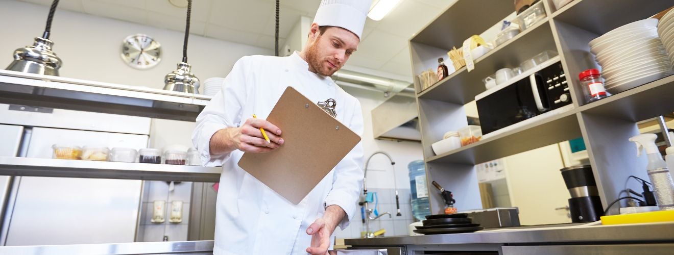 A chef with a clipboard checking over critical food safety points.