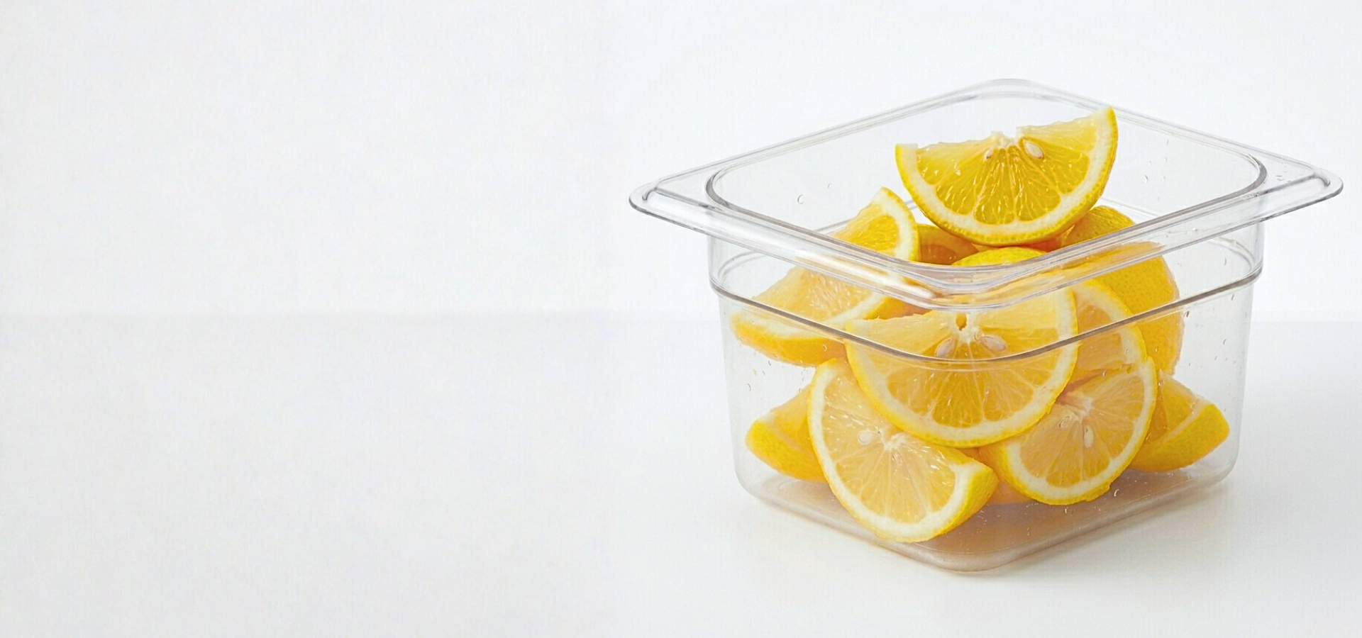 Clear Cambro food storage container filled with sliced lemons on a white background.