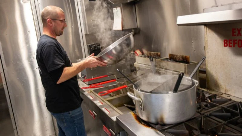 Person working in a kitchen with steam rising from a pot on a stove.