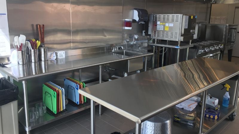 Commercial kitchen prep area with stainless steel worktables, sink, cutting boards, and small cooking equipment