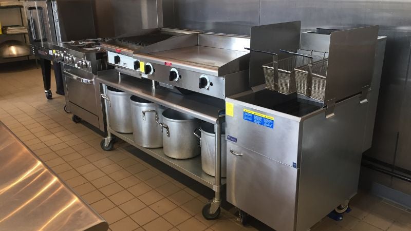 Commercial kitchen cookline with flat top griddle, fryer, range, and stock pots in culinary training facility