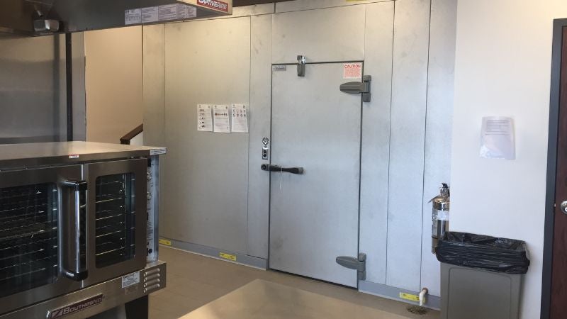Commercial kitchen walk-in cooler door next to convection oven in culinary training facility