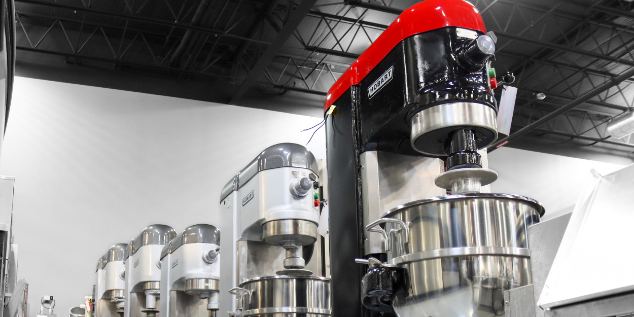 A row of professionally refurbished commercial planetary mixers in a warehouse setting.