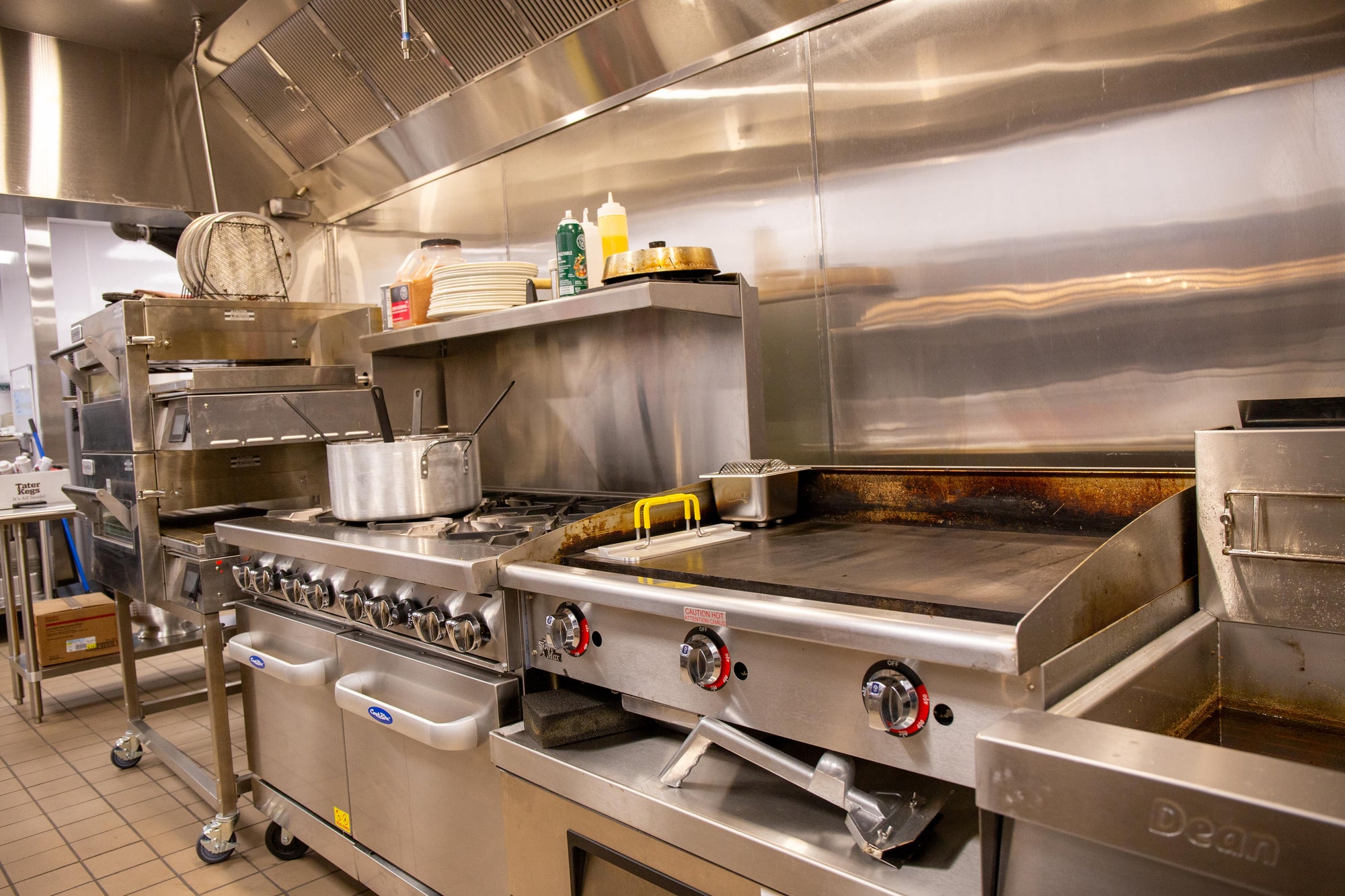 Commercial kitchen cooking line with griddle, range, fryer and ventilation hood