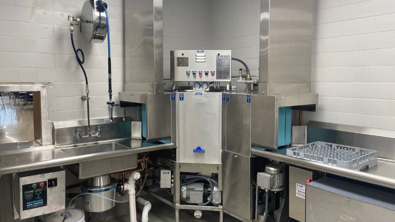School cafeteria dishwashing station with commercial dishwasher, sinks, and plumbing system