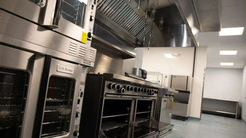 Commercial kitchen cookline with ovens, range, and stainless steel ventilation hood