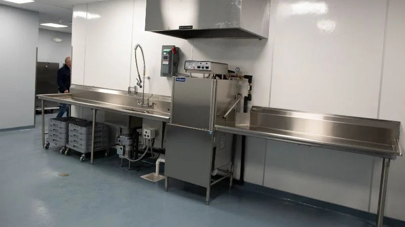 Commercial dishwashing area with sinks, dish machine, and stainless steel work tables