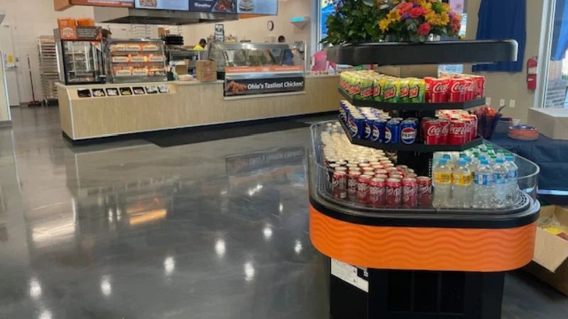 Front-of-house convenience store interior featuring hot food service counter with menu boards, heated display case, and central grab-and-go beverage island