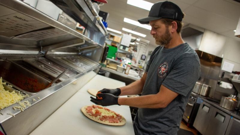 Staff assembling pizza with toppings at prep station