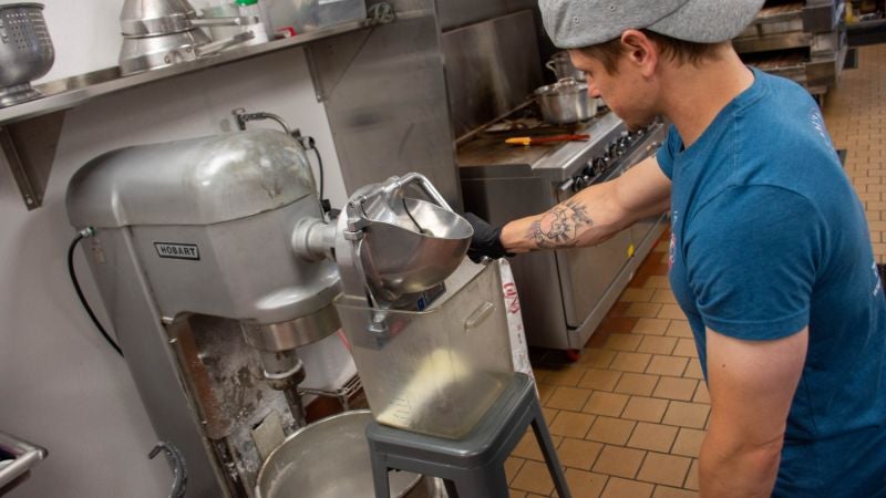 Staff operating a commercial dough mixer with flour feed attachment in prep area