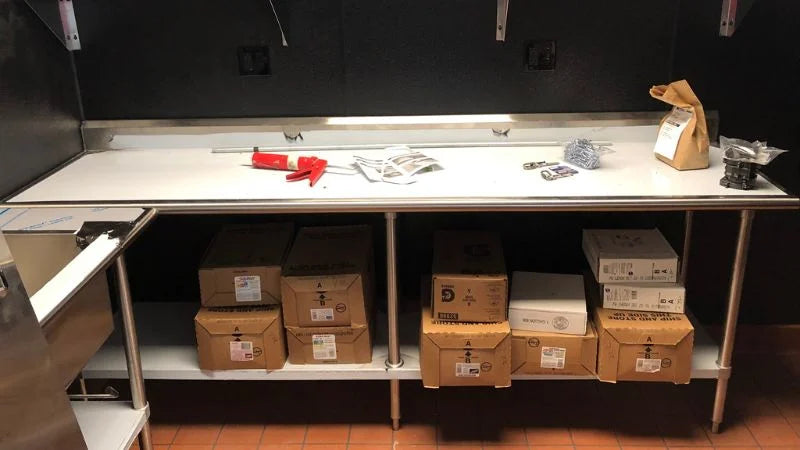 Stainless steel prep counter with under-shelf storage holding boxes and small tools on the work surface