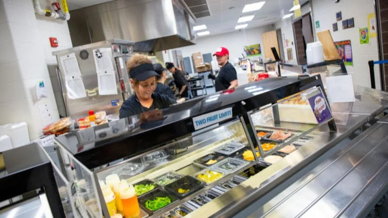 People working in a kitchen with a salad bar in the foreground