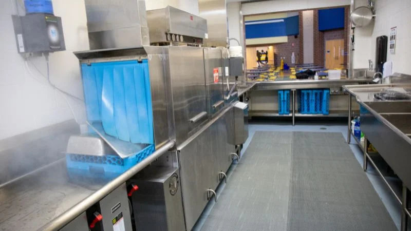Commercial dishwashing area with conveyor dish machine and clean tray storage in school kitchen