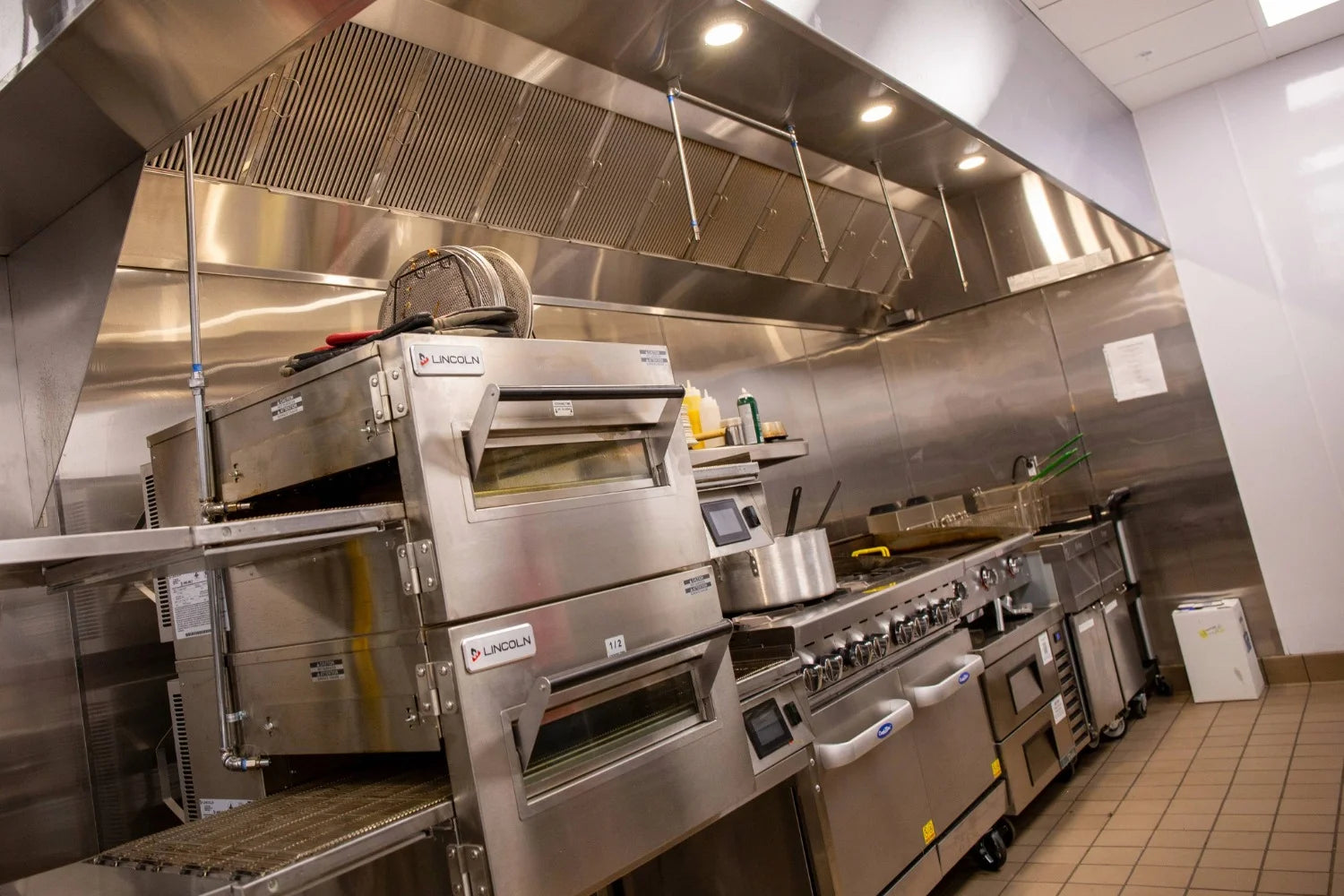 Stacked Lincoln conveyor ovens integrated into commercial cook line under exhaust hood
