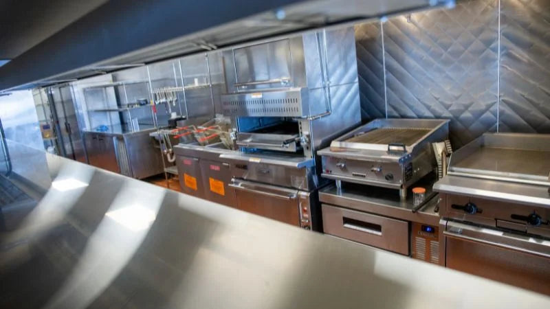 Commercial kitchen with stainless steel appliances and a tiled wall.