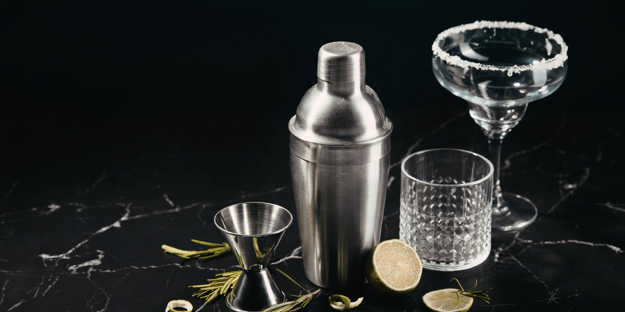 Cocktail shaker and bar supplies set with glassware on marble surface