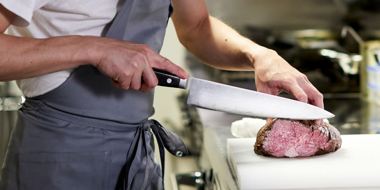 Chef slicing cooked steak with sharp kitchen cutlery on cutting board