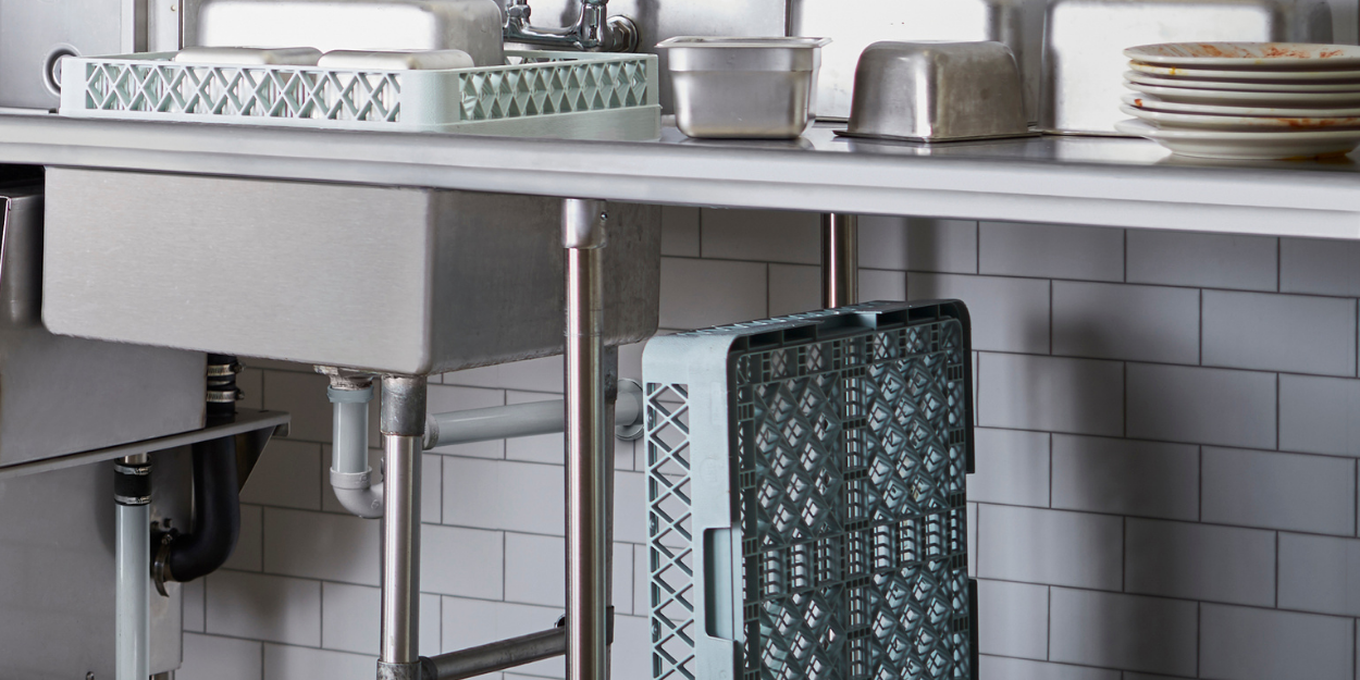 Professional commercial dish room workspace featuring stainless steel sinks, heavy-duty shelving, and dish rack storage solutions