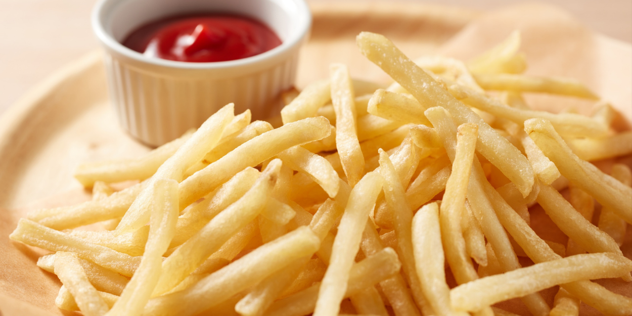 A golden portion of crispy, thin-cut french fries served on a wooden board with a side of ketchup in a white ramekin