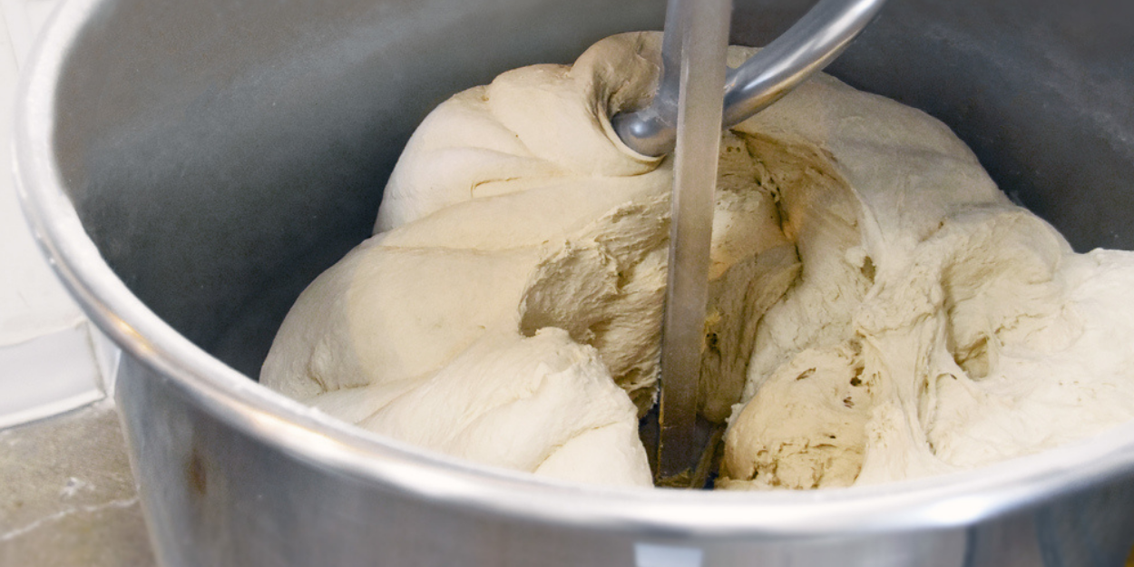 Commercial dough mixer kneading bread dough in stainless steel mixing bowl
