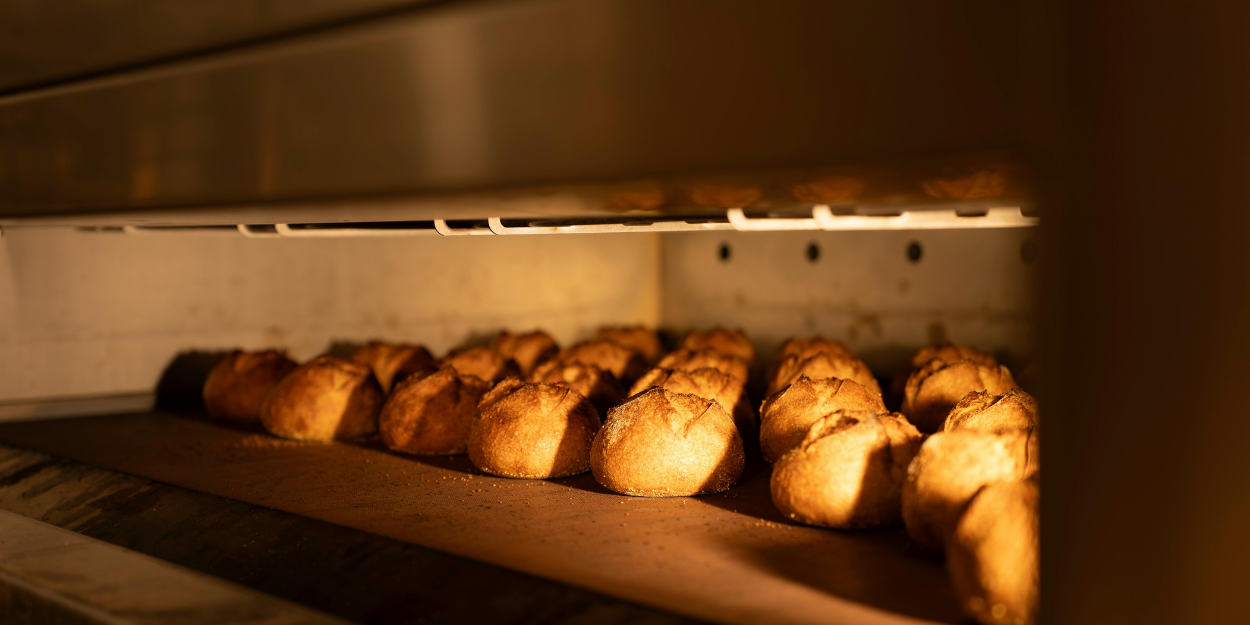 A row of freshly baked artisan bread rolls cooling inside a heavy-duty commercial deck oven.