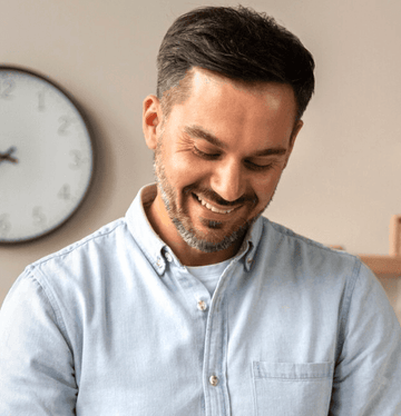 Man wearing a light blue shirt with a clock in the background.