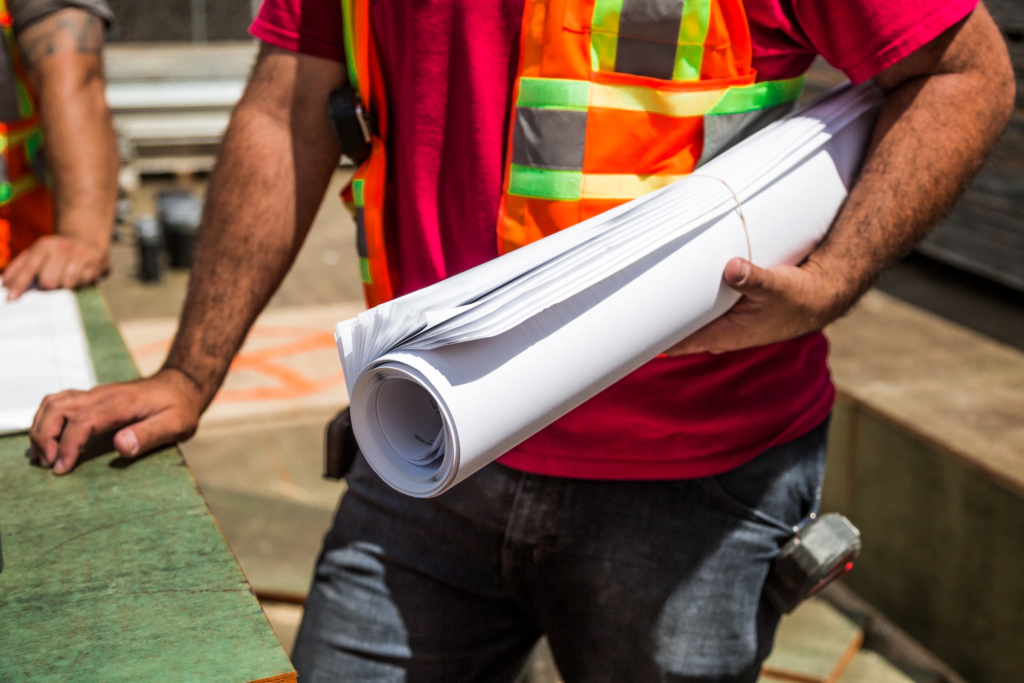 Construction worker holding rolled building plans at job site wearing high-visibility safety vest