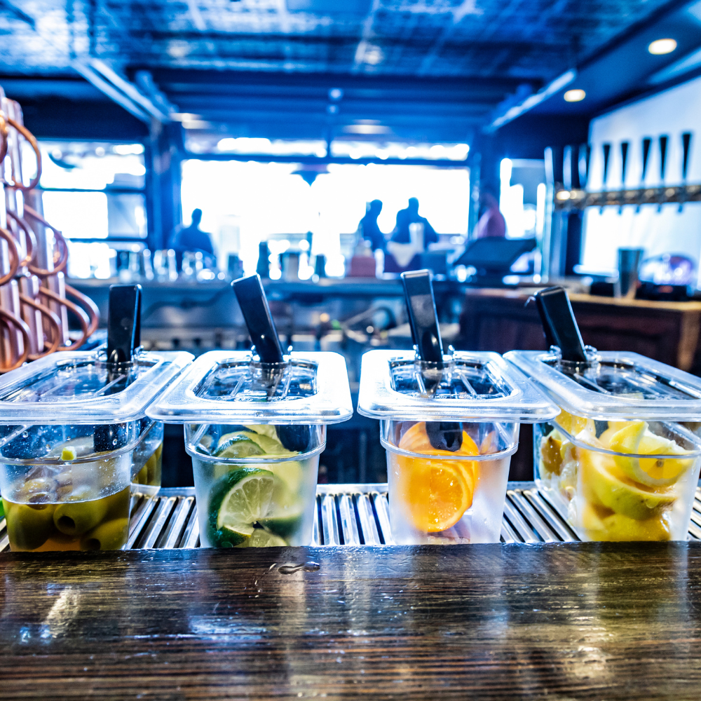 Clear Cambro food pans on a bar counter with a blurred bar background.