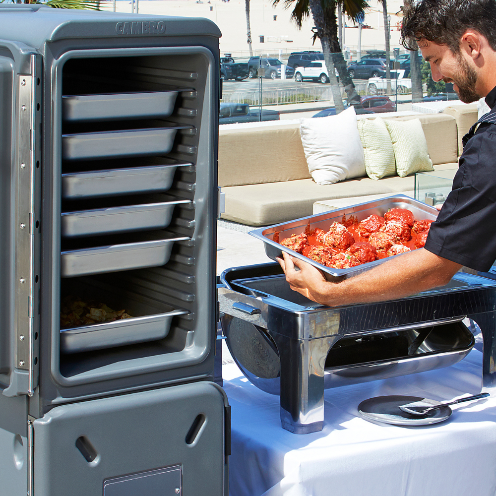 Person moving a filled food pan from a Cambro food carrier into a chafing dish