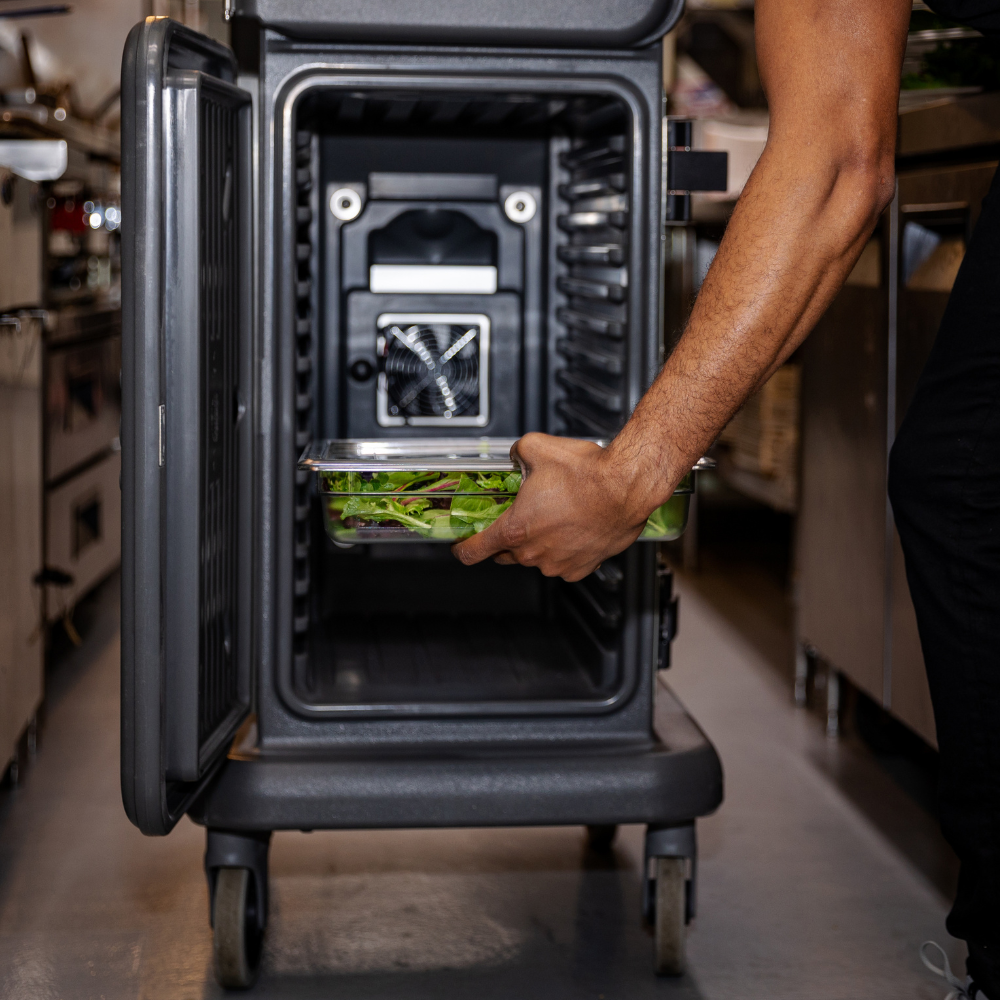 Person placing a food pan filled with greens into a Cambro food carrier