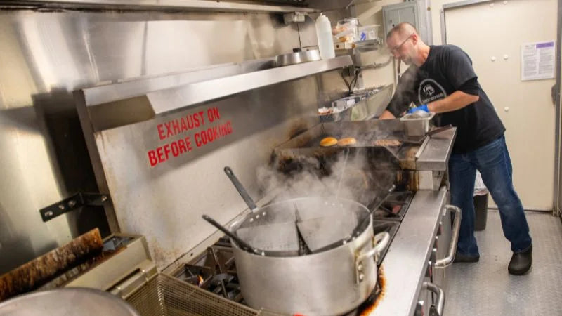 Person working in a commercial kitchen with exhaust system warning sign.