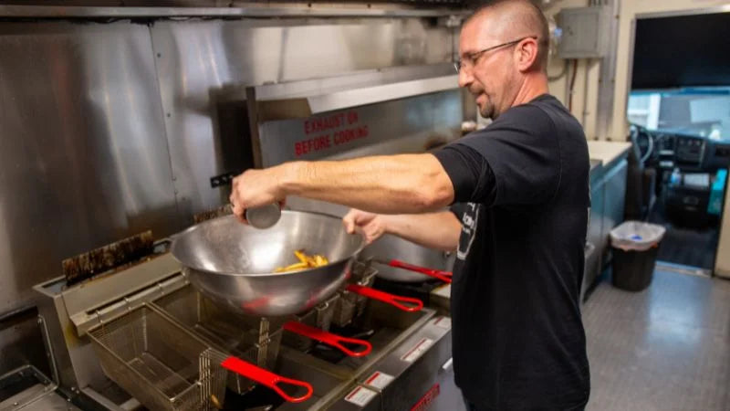 Person cooking in a commercial kitchen with a large metal wok.