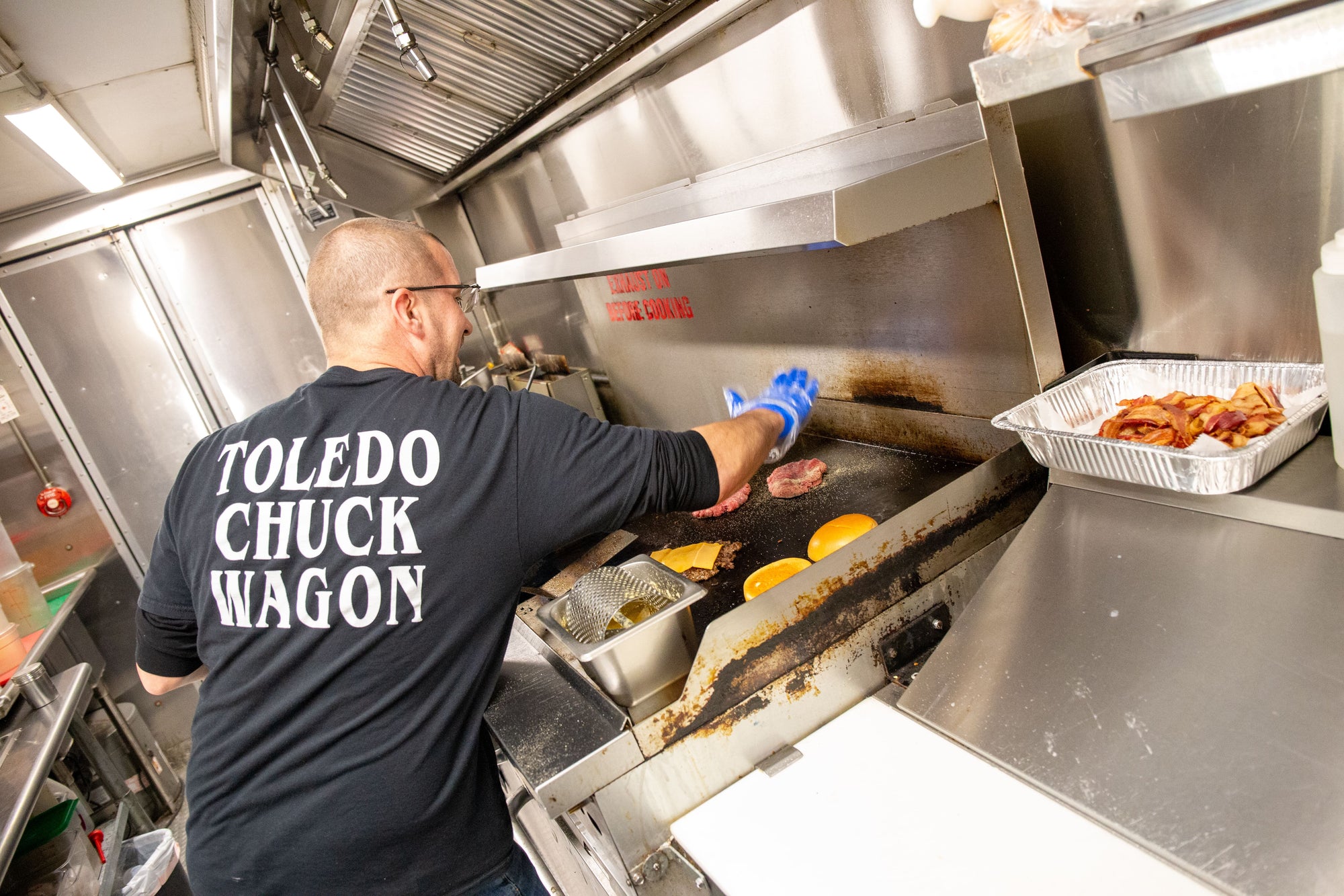 Chef cooking burgers in a food truck wearing a shirt that says "Toledo Chuck Wagon"