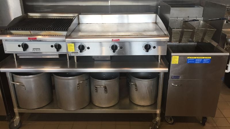 Commercial kitchen cookline with charbroiler, flat top griddle, fryer, and stock pots in culinary training kitchen