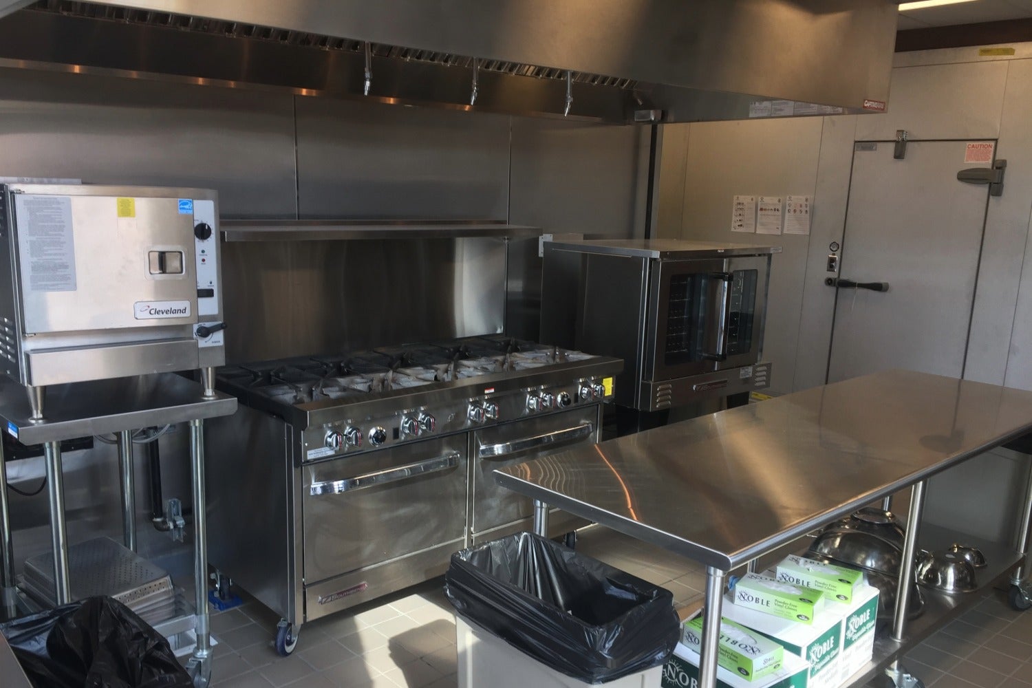Commercial kitchen cookline with gas range, convection oven, steam oven, and stainless steel prep table