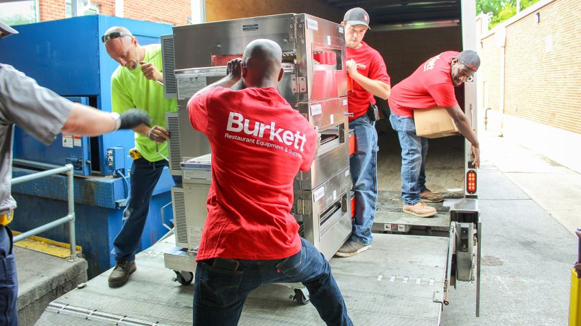 Burkett delivery team installing commercial kitchen equipment from truck at restaurant loading dock