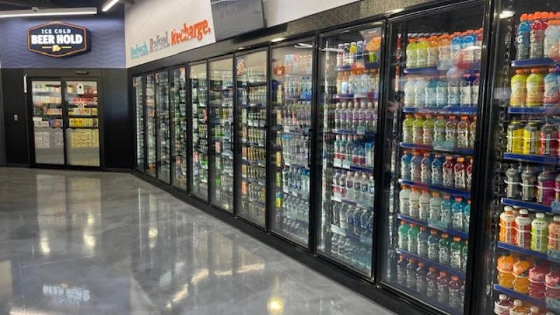 Glass-door beverage cooler lineup featuring self-serve refrigerated drinks and beer cave entrance