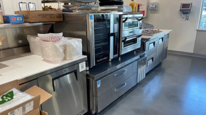 Back-of-house prep line with high-speed ovens, undercounter refrigeration drawers, and stainless prep workspace