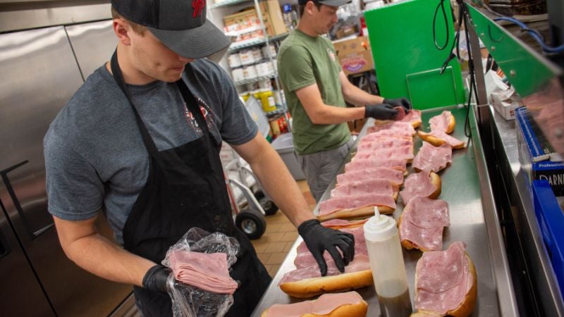 Kitchen staff assembling sandwiches on a prep line with stainless work surface and ingredient staging