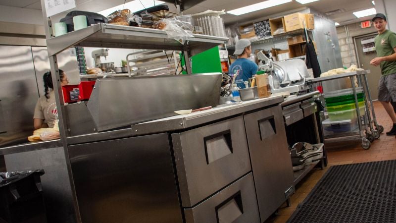 Pizza prep line with refrigerated base, ingredient rail, and staff working in background