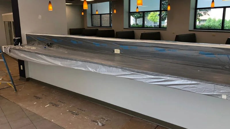 Long service counter covered in protective plastic during renovation, with booth seating and pendant lights in the background
