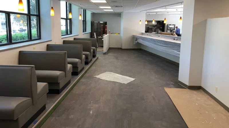Dining area with booth seating along windows and a long service counter covered in plastic during renovation