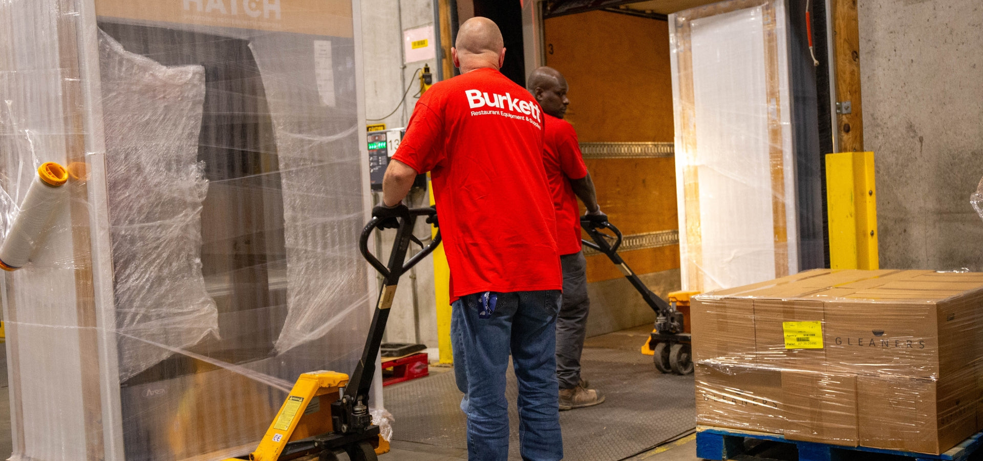 Burkett Restaurant Equipment team member using a pallet jack to move a wrapped HATCH for Hunger refrigerated merchandiser.
