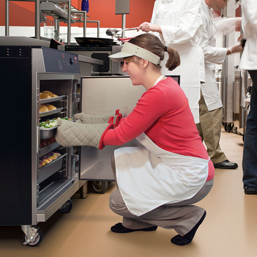 Hatco mobile stainless steel heated holding cabinet being loaded with food trays during kitchen prep.