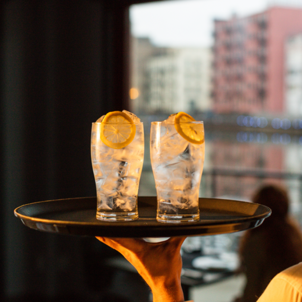 two glasses of ice and water with lemons. A hand carrying the glasses on a serving tray.