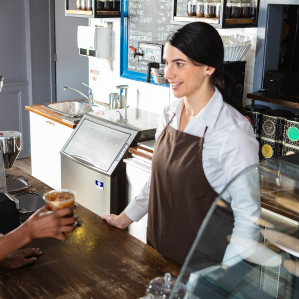 Worker serving ice coffee to a customer with an ice machine in the background
