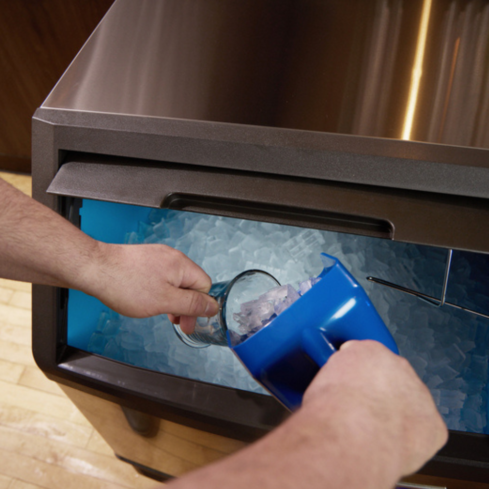 a blue ice scoop being used to pour ice into a glass cup inside an ice machine
