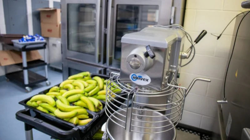Bananas on a tray in front of a food processing machine in a kitchen setting