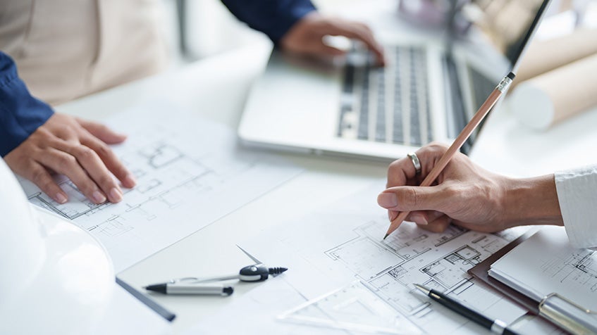 Planning commercial kitchen layout with blueprints and laptop on desk