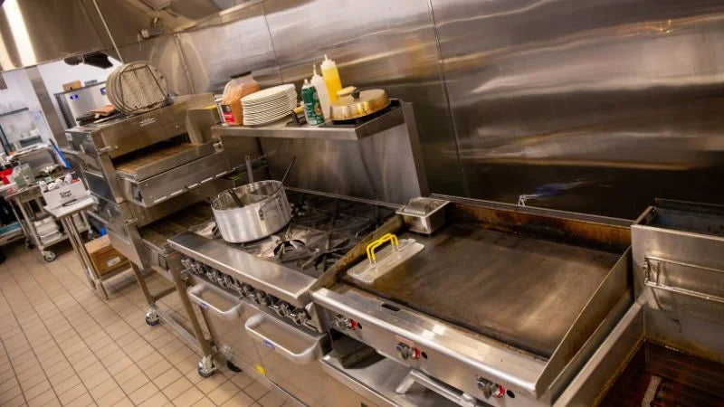 Commercial kitchen cook line with griddle, gas range, fryer, and stainless backsplash